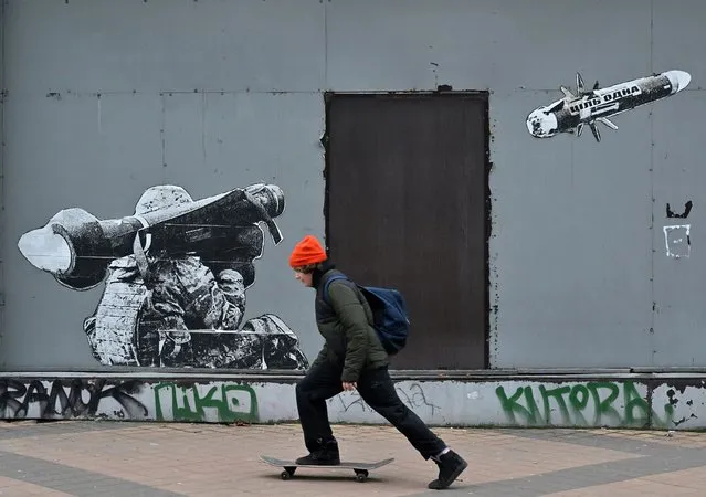 A boy skateboards along a graffiti on a wall depicting a Ukrainian soldier firing a portable anti-tank missile system, in Kyiv on January 25, 2023, amid the Russian invasion of Ukraine. (Photo by Sergei Supinsky/AFP Photo)