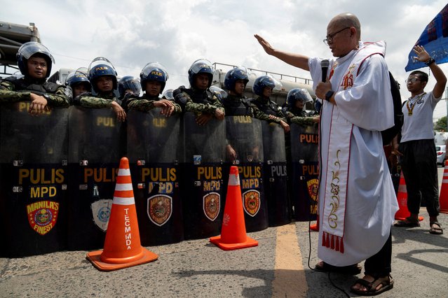 Catholic priest Robert Reyes raises his hand as he prays over the police officers blocking protesters from marching during a protest calling for fair elections, a day after the midterm elections, in Manila, Philippines on May 13, 2025. (Photo by Lisa Marie David/Reuters)
