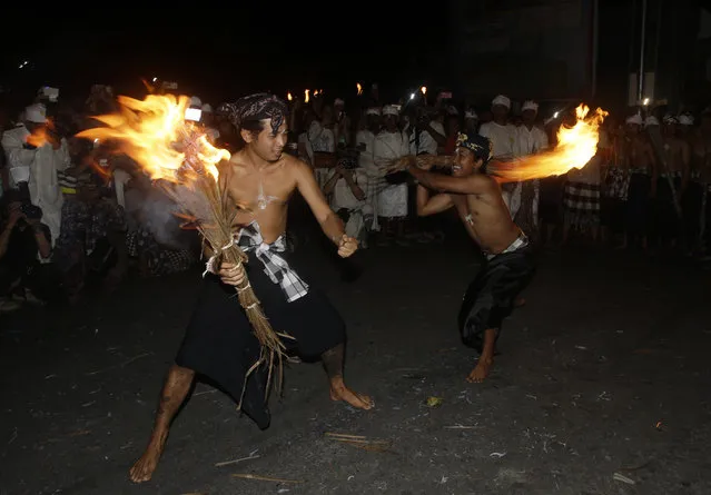 Balinese men fight with flaming coconut leaves during the fire fight ritual called 'Lukat Gni' before Nyepi, the annual day of silence marking Balinese Hindu new year, in Klungkung, Bali, Indonesia, Friday, March 16, 2018. (Photo by Firdia Lisnawati/AP Photo)