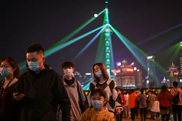 People wearing face masks as a preventive measure against the COVID-19 coronavirus walk on The Bund in Shanghai on November 2, 2020, while is seen a light show in the financial district of Lujiazu. (Photo by Hector Retamal/AFP Photo)