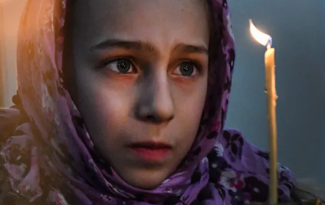 A girl looks on candle during an Orthodox Christmas service in a church in Bishkek late on January 6, 2018. Orthodox Christians celebrate Christmas on January 7 in the Middle East, Russia and other Orthodox churches that use the old Julian calendar instead of the 17th-century Gregorian calendar adopted by Catholics, Protestants, Greek Orthodox and commonly used in secular life around the world. (Photo by Vyacheslav Oseledko/AFP Photo)
