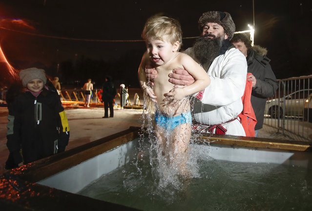A man dips a boy in ice water during a traditional Epiphany celebration in St. Petersburg, Russia, late Monday, January 18, 2021. Thousands of Russian Orthodox Church followers plunged into rivers and ponds across the country to mark the Epiphany, cleansing themselves with water deemed holy for the day. (Photo by Dmitri Lovetsky/AP Photo)