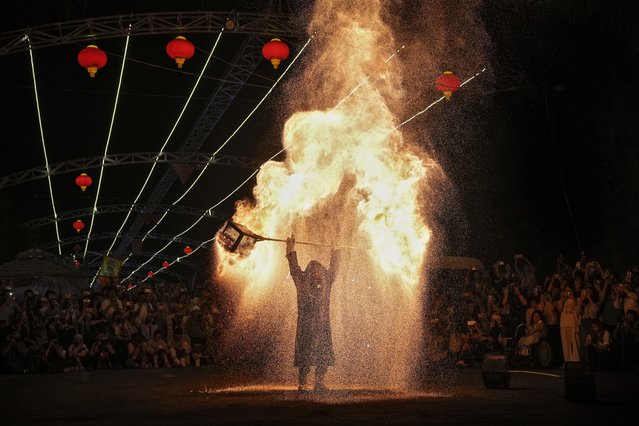 People watch an artist performs a fire kettle show during the Mid-Autumn Festival at a night market in Beijing, Tuesday, September 17, 2024. (Photo by Andy Wong/AP Photo)