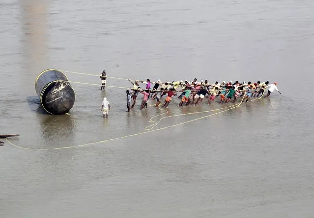 Labourers pull a pontoon to construct a temporary bridge for the Magh Mela festival on the river Ganges in Allahabad, India, December 15, 2015. The festival is an annual religious event held during the Hindu month of Magh, when thousands of Hindu devotees take a holy dip in the waters of the Ganges. (Photo by Jitendra Prakash/Reuters)