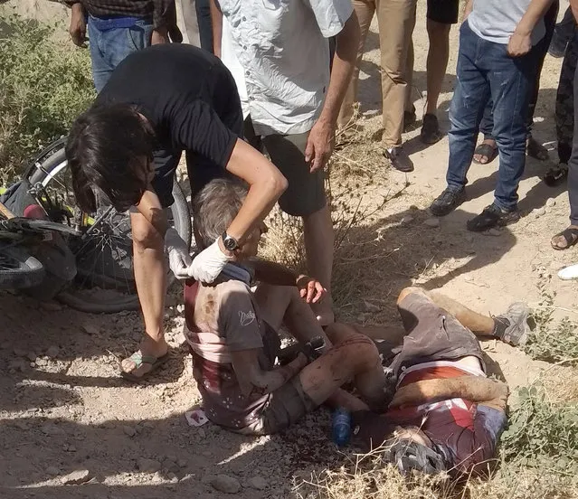 In this photo taken on Sunday, July 29, 2018, a woman helps a wounded cyclist, where the four tourists were killed when a car rammed into a group of foreigners on bicycles south of the capital of Dushanbe, Tajikistan. The Islamic State group on Tuesday claimed responsibility for a car-and-knife attack on Western tourists cycling in Tajikistan that killed two Americans and two Europeans. (Photo by Zuly Rahmatova/AP Photo)