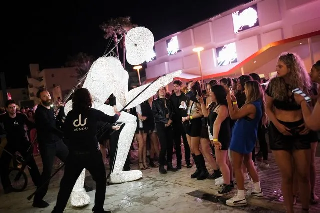 A team of five puppeteers control an LED-lit Dundu puppet created by German doll maker Tobias Husemann as tourists wait to enter the Hi Ibiza nightclub near Playa d'en Bossa, in Ibiza, Spain on May 1, 2022. (Photo by Nacho Doce/Reuters)