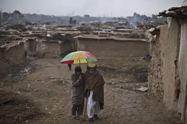 A youth holds an umbrella to shelter an elderly man from rain in a slum that hosts Afghan refugees and internally displaced Pakistanis from tribal areas, on the outskirts of Islamabad, Pakistan, Saturday, February 7, 2015. (Photo by Muhammed Muheisen/AP Photo)