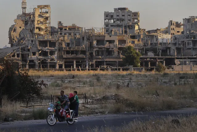 People ride their motorcycle by damaged buildings in the old town of Homs, Syria, Wednesday, August 15, 2018. The Russian Defense Ministry said Wednesday it is coordinating efforts to help Syrian refugees return home and rebuild the country's infrastructure destroyed by the civil war. (Photo by Sergei Grits/AP Photo)
