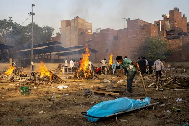 A man prepares a funeral pyre to cremate the body of a person, who died due to the coronavirus disease (COVID-19), at a crematorium ground in New Delhi, India, April 22, 2021. (Photo by Danish Siddiqui/Reuters)