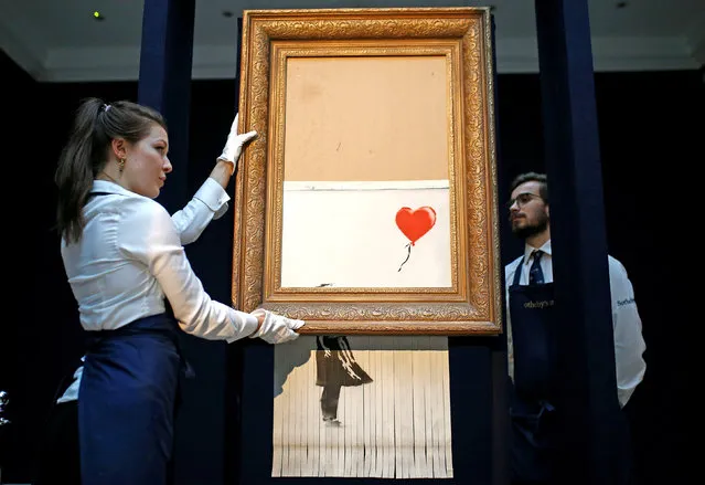 Staff from Sotheby's auctioneers reposition Banksy’s Love is in the Bin, which is now half-shredded, in London, Britain, October 12, 2018. (Photo by Henry Nicholls/Reuters)