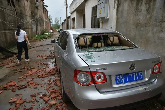 A woman walks past a damaged car after a tornado hit the city of Suqian, in China's eastern Jiangsu province on September 20, 2023. (Photo by AFP Photo/China Stringer Network)