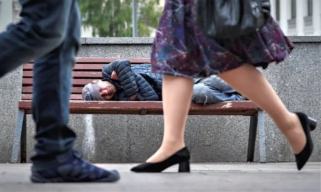 People walk by a man sleeping on a bench in a street in Moscow, Russia 07 June 2021. (Photo by Yuri Kochetkov/EPA/EFE)