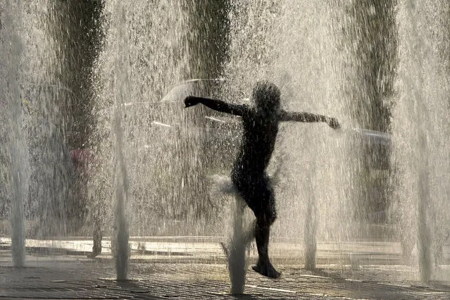 A boy cools off in a fountain at a park as summer-like temperatures move into the region Saturday, June 5, 2021, in Kansas City, Mo. (Photo by Charlie Riedel/AP Photo)