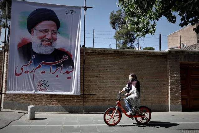 An Iranian girl rides a bicycle next to a huge poster depicting Iranian presidential conservative candidate Ebrahim Raisi, in Tehran, Iran, 30 May 2021. Iranians will vote in a presidential election on 18 June 2021. (Photo by Abedin Taherkenareh/EPA/EFE)