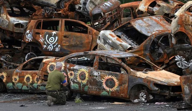A Ukrainian serviceman crosses himself at the symbolic cemetery of cars shot by Russian troops, some painted by local artists, in Irpin, on August 9, 2022, amid Russian invasion of Ukraine. (Photo by Sergei Supinsky/AFP Photo)