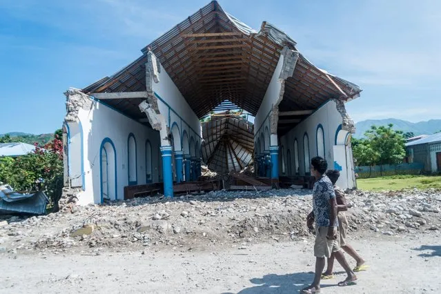 Two Haitians walk past a church destroyed during an earthquake in Les Anglais on August 14, 2021. At least 1,297 people were killed in the 7.2-magnitude quake that struck Saturday about 100 miles (160 kilometers) to the west of the densely populated capital Port-au-Prince, which was devastated in a massive 2010 quake. (Photo by Reginald Louissaint Jr./AFP Photo)