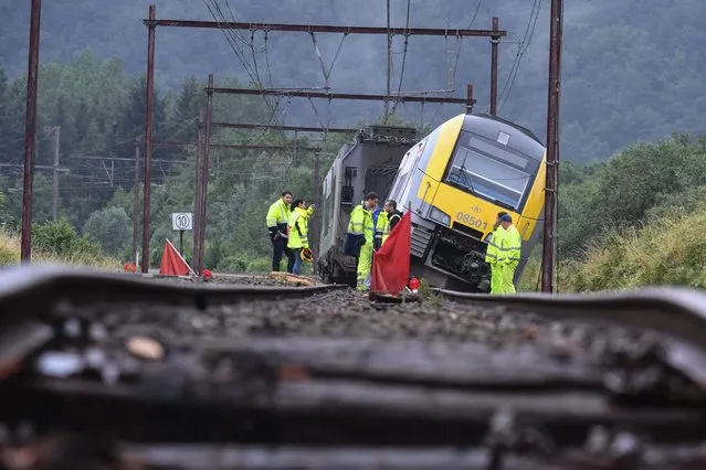 Rail workers stand near a derailed carriage belonging to the Belgium SNCB train service, the day after heavy rains and floods near the town of Rochefort on July 16, 2021. The death toll in Belgium has jumped to 15 with more than 21,000 people left without electricity in one region. The death toll from devastating floods in Europe soared to at least 108 on July 16, 2021, most in western Germany where emergency responders were frantically searching for missing people. (Photo by John Thys/AFP Photo)