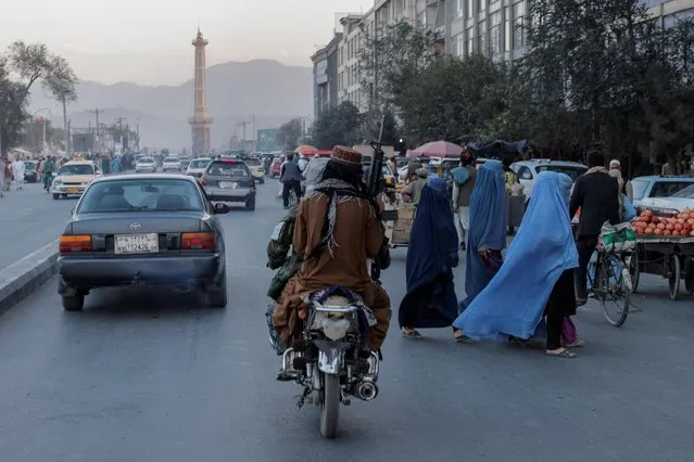 A group of women wearing burqas crosses the street as members of the Taliban drive past in Kabul, Afghanistan October 9, 2021. (Photo by Jorge Silva/Reuters)