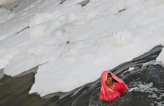 A Hindu woman worships the Sun god as she stands amidst the foam covering the polluted Yamuna river during the Hindu religious festival of Chhath Puja in New Delhi, India, November 10, 2021. (Photo by Adnan Abidi/Reuters)
