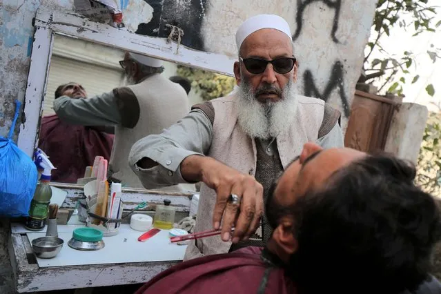 A barber shaves a customer's beard at a roadside shop, during the World AIDS Day in Peshawar, Pakistan, 01 December 2021. According to doctors, cuts from razor blades that haven't undergone proper sterilization are among some of the main causes of AIDS spread. World AIDS Day, observed annually on 01 December, is dedicated to raising awareness against the spread of AIDS and HIV infections. (Photo by Arshad Arbab/EPA/EFE)