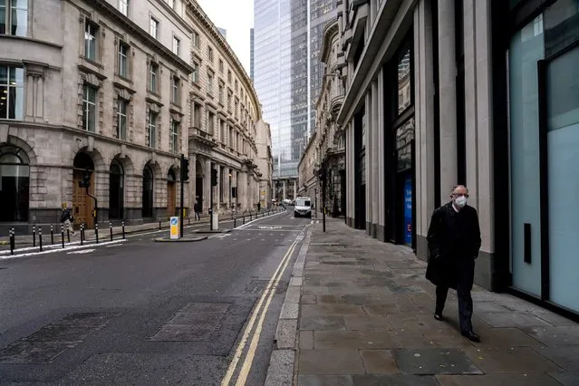 A man wears a face mask while walking in an empty street in the financial district, known as The City, in London, Monday, December 13, 2021. While many people will re-start working from home, the British government raised the country's official coronavirus threat level on Sunday, warning the rapid spread of omicron “adds additional and rapidly increasing risk to the public and health care services” at a time when COVID-19 is already widespread. (Photo by Alberto Pezzali/AP Photo)