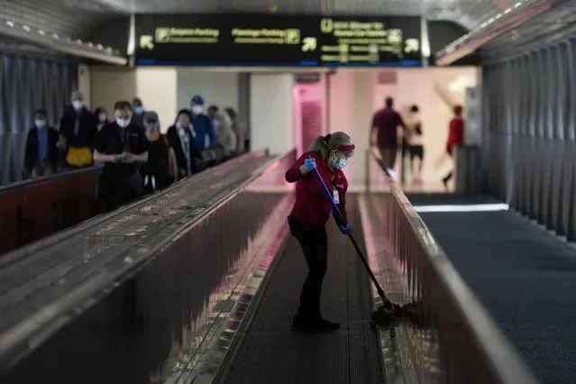 An airport employee cleans the sides of a moving walkway at Miami International Airport, Monday, December 27, 2021, in Miami. Thousands of flights worldwide were canceled or delayed on Monday, as airline staffing shortages due to the rapid spread of the omicron variant of COVID-19 continued to disrupt the busy holiday travel season. (Photo by Rebecca Blackwell/AP Photo)