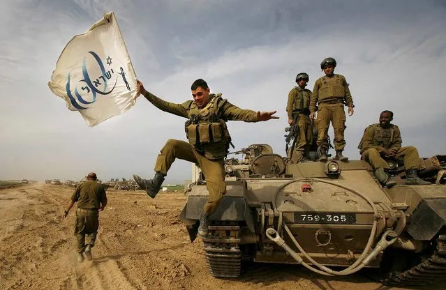 An Israeli soldier jumps off an armored vehicle carrying a flag of Israel's 60th anniversary as he celebrates with his unit their return from the Gaza Strip on the Israeli side of the border, Jan. 16, 2009. (Photo by Anja Niedringhaus/AP Photo)