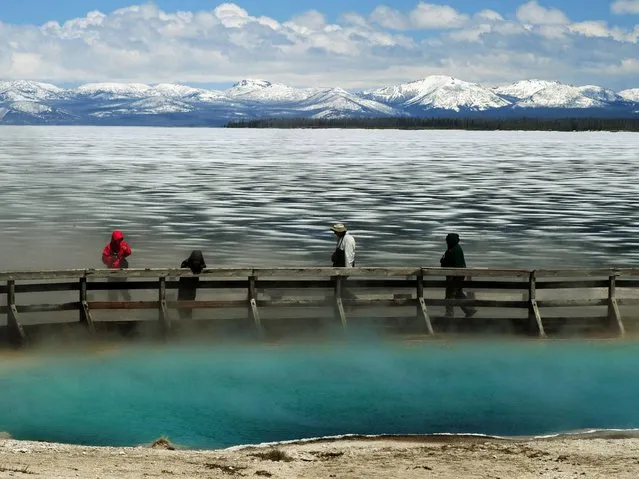 Tourists walk beside a hot spring and the partially frozen Yellowstone Lake at the West Thumb Geyser Basin in the Yellowstone National Park. (Photo by Mark Ralston/AFP Photo)