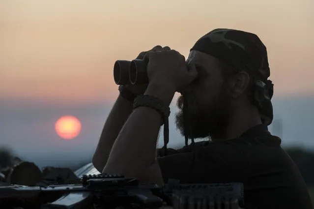 In this photo taken Monday, June 22, 2015, a Ukrainian serviceman from the Kiev-2 volunteer battalion uses binoculars at the frontline in the village of Krymske, east Ukraine. (Photo by Evgeniy Maloletka/AP Photo)