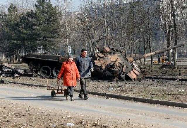 People walks past a tank destroyed in fighting during Ukraine-Russia conflict, in the besieged southern port of Mariupol, Ukraine on March 23, 2022. (Photo by Alexander Ermochenko/Reuters)