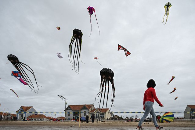 A woman walks past flying kites during the 29th edition of the International Kite and Wind Festival as kite flyers from all over France and abroad gather in Chatelaillon-Plage, south-western France, on April 10, 2023. (Photo by Philippe Lopez/AFP Photo)