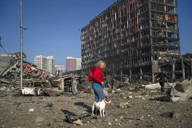 Irina Zubchenko walks with her dog Max amid the destruction caused after shelling of a shopping center, in Kyiv, Ukraine, Monday, March 21, 2022. (Photo by Rodrigo Abd/AP Photo)