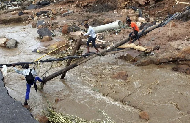 People walk across a makeshift bridge over a river, after a bridge was swept away in Ntuzuma, outside Durban, South Africa, Tuesday, April 12, 2022. Prolonged rains and flooding in South Africa's KwaZulu-Natal province have claimed the lives of at least 20 people, according to local officials. (Photo by AP Photo/Stringer)