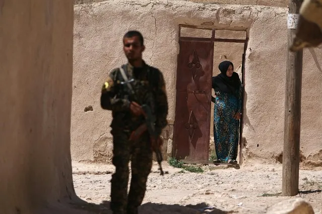 A Syria Democratic Forces (SDF) fighter stands near a woman looking out a doorway in a village, on the outskirts of Manbij city, after they took control of it from Islamic State forces, Aleppo province, Syria June 8, 2016. (Photo by Rodi Said/Reuters)