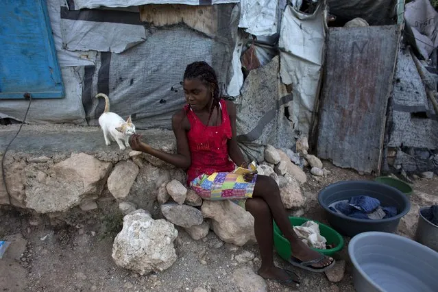 In this June 26, 2015 photo, a young woman shares a cracker with a kitten in a post-earthquake tent camp that residents are hoping to turn into a permanent neighborhood in Port-au-Prince, Haiti. More than five years after a magnitude 7.0 quake destroyed much of the capital, there are few visible signs of the disaster and the vast majority of the people who were displaced have found homes. (Photo by Rebecca Blackwell/AP Photo)