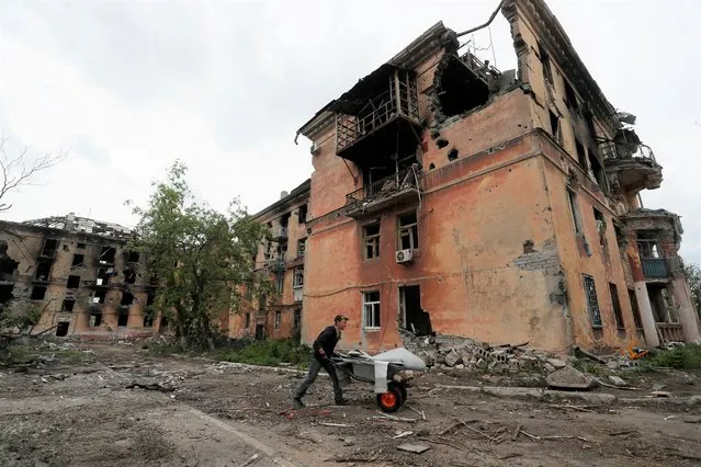 A local resident pushes a wheelbarrow past a heavily damaged apartment building near Azovstal Iron and Steel Works, during Ukraine-Russia conflict in the southern port city of Mariupol, Ukraine on May 22, 2022. (Photo by Alexander Ermochenko/Reuters)