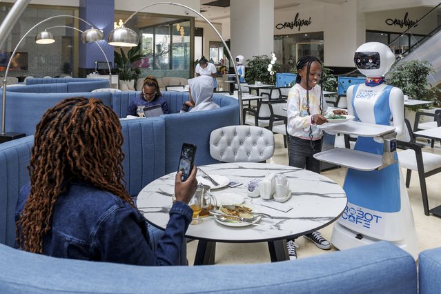 A young patron retreives her meal order from a robotic waiter's tray at the Robot Cafe, Kenya's first restaurant to employ humanoid robots as waiters, in Nairobi on August 27, 2024. Working alongside human staff, the robots are programmed with artificial intelligence and controlled remotely to provide services that include calling out welcomes to approaching patrons, serving up non-spillable orders and even belting out 'happy birthday' music on appropriate occassion. (Photo by Tony Karumba/AFP Photo)