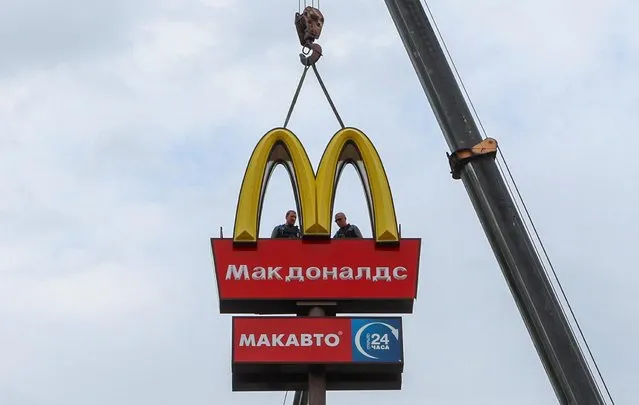 Workers use a crane to dismantle the McDonald's Golden Arches while removing the logo signage from a drive-through restaurant of McDonald's in the town of Kingisepp in the Leningrad region, Russia on June 8, 2022. McDonald's last month said it was selling its restaurants in Russia to one of its local licensees, Alexander Govor. The deal marked one of the most high-profile business departures since Russia sent tens of thousands of troops into Ukraine on Feb. 24. (Photo by Anton Vaganov/Reuters)