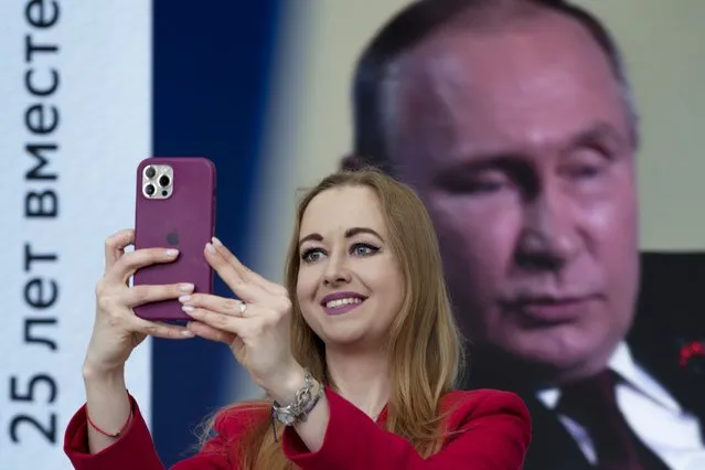 A participant takes a selfie as Russian President Vladimir Putin speaks at a plenary session of the St. Petersburg International Economic Forum in St.Petersburg, Russia, Friday, June 17, 2022, with the words reading “25 years together”. Russia’s annual event to tout its investment opportunities this year was shadowed by the stern international sanctions imposed on the country after the Kremlin sent troops into Ukraine four months earlier and by the extensive disapproval of foreign businesses, which have suspended operations or pulled out entirely, leaving Russian shopping centers pocked with dark, shuttered stores. (Photo by Dmitri Lovetsky/AP Photo)