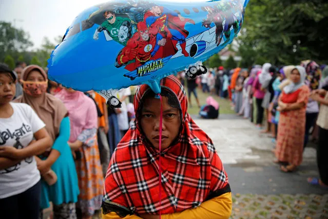A woman holds a baloon as she queues to buy government-subsidised beef at Cilincing district in Jakarta, Indonesia, June 29, 2016. (Photo by Reuters/Beawiharta)