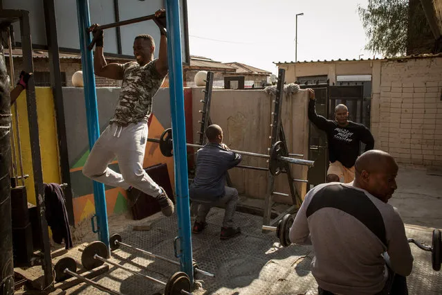 Sandi Makama (L), 40, does pull-ups while others join exercises in the early morning hours at the iKasi Gym in the Township of Alexandra, Johannesburg, South Africa, 16 September 2022. The gym was originally part of owner Tumi Masite's house, but it has now expanded into the front garden. The gym is situated only some 100 meters from the house the late Nelson Mandela used to live in. It caters to the local community, which has a 50 percent unemployment rate, and households with an average income of 1,950 US dollar per year. By emphasizing a holistic approach to bodybuilding, the gym offers opportunities for both mental and physical improvement, with trainers stressing the importance of discipline and providing opportunities to develop job skills. (Photo by Kim Ludbrook/EPA/EFE)
