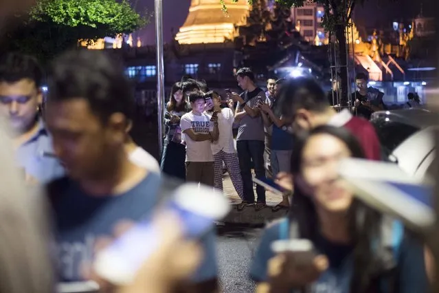 In this picture taken on August 10, 2016, residents of Yangon gather in the street near the city hall to play Pokemon Go on their smartphones. While Myanmar was officially excluded from the August 6 Pokemon Go launch in Southeast Asia, game fanatics have discovered Pokemon Go is active in Yangon, immediately attracting crowds of players and turning several historical landmarks into hunting grounds. (Photo by Ye Aung Thu/AFP Photo)