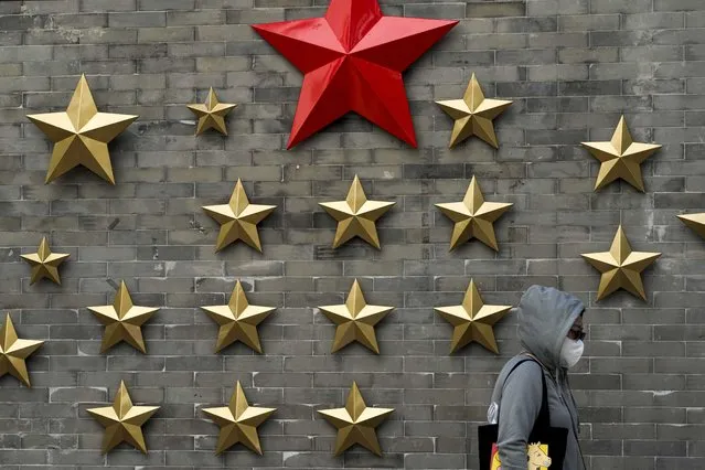 A woman wearing a face mask walks by communist symbol of a stars on display outside a restaurant in Beijing, Sunday, October 9, 2022. (Photo by Andy Wong/AP Photo)