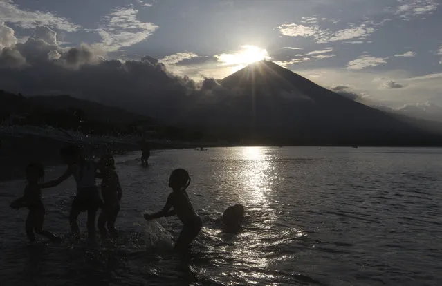 Children play at a beach with the Mount Agung volcano seen in the background during the sunset in Karangasem, Bali, Indonesia, Sunday, October 8, 2017. More than 140,000 people have fled from the surrounds of Mount Agung since authorities raised the volcano's alert status to the highest level after a sudden increase in tremors. It last erupted in 1963, killing more than 1,000 people. (Photo by Firdia Lisnawati/AP Photo)