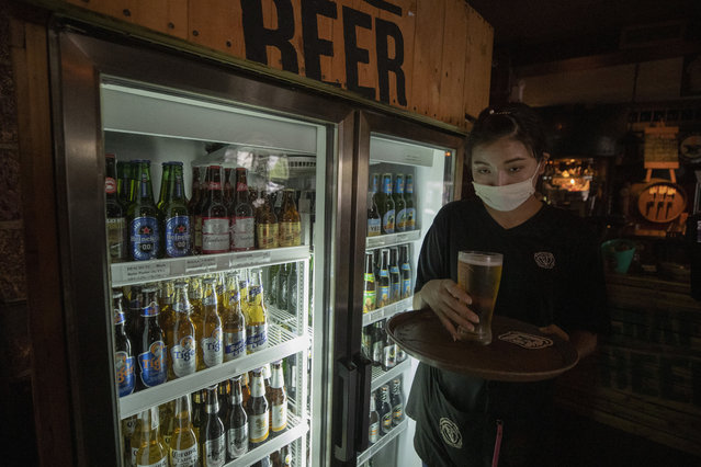 A worker wearing a face mask to help curb the spread of the coronavirus as she serves beer to a customer at Roadhouse Barbecue restaurant in Bangkok, Thailand, Monday, June 15, 2020. Restaurants will no longer be banned from serving alcohol. Thai government continues to ease restrictions related to running business in capital Bangkok that were imposed weeks ago to combat the spread of COVID-19. (Photo by Sakchai Lalit/AP Photo)