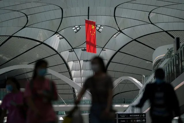 People wearing face masks following the coronavirus disease (COVID-19) outbreak walk under a Chinese flag at Beijing Daxing International Airport in Beijing, China on July 24, 2020. (Photo by Thomas Suen/Reuters)