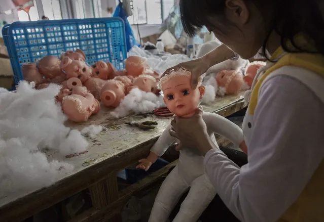 A Chinese worker puts a head on a doll at a toy factory on September 17, 2015 in Xietang, Zhejiang Province, China. Many of the toy factories in the area have seen a sharp decrease in orders from Europe and Latin America in 2015, with many saying that a decline in Russia's currency and inflation in South America being the main reason. (Photo by Kevin Frayer/Getty Images)