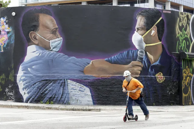 A construction worker rides a scooter past a mural by Hiero Veiga of billionaire businessman Moishe Mana, left, and City of Miami Mayor Francis X. Suarez wearing masks Monday, July 13, 2020, in the Wynwood Arts District of Miami. Florida's rapidly increasing number of coronavirus cases is turning Miami into the “epicenter of the pandemic”, a top doctor warned Monday, while an epidemiologist called the region's situation “extremely grave”. (Photo by Wilfredo Lee/AP Photo)