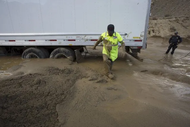 A worker walks through mud while preparing to pull a truck mired in mud and debris on State Route 58 near Tehachapi, California, about 60 miles (97 km) outside of Los Angeles October 17, 2015. (Photo by David McNew/Reuters)