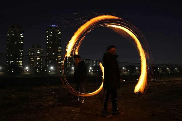 People twirl cans with holes filled with burning wood chips and straw to celebrate the first full moon of the Lunar New Year, in Seoul, South Korea, Saturday, February 4, 2023. According to the lunar calendar, the first full moon falls on Feb. 5 this year. (Photo by Lee Jin-man/AP Photo)